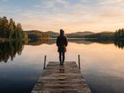 Moving to Finland: The Complete 2026 Guide for Students, Workers, and Families Traveler standing on a wooden dock overlooking a calm Finnish lake surrounded by pine forest at golden hour