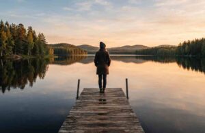 Moving to Finland: The Complete 2026 Guide for Students, Workers, and Families Traveler standing on a wooden dock overlooking a calm Finnish lake surrounded by pine forest at golden hour